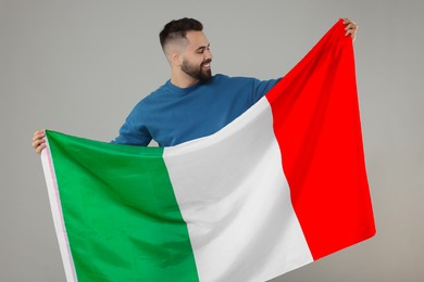 Young man holding flag of Italy on light grey background