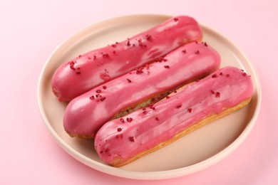 Photo of Delicious eclairs covered with glaze on pink background