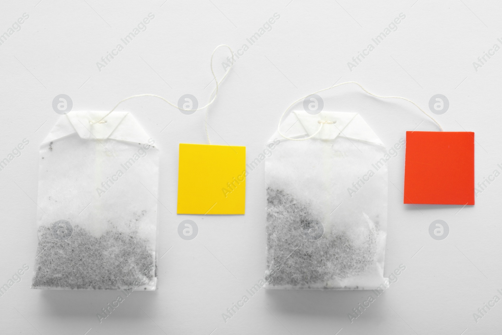 Photo of Unused tea bags with tags on white background, top view. Space for text