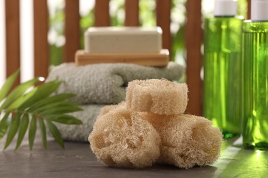 Photo of Loofah sponges, towels, soap, cosmetic products on grey table, selective focus