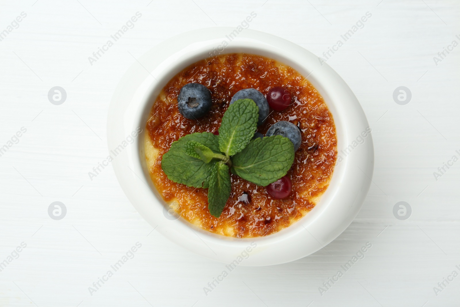 Photo of Delicious creme brulee with berries and mint in bowl on white wooden table, top view