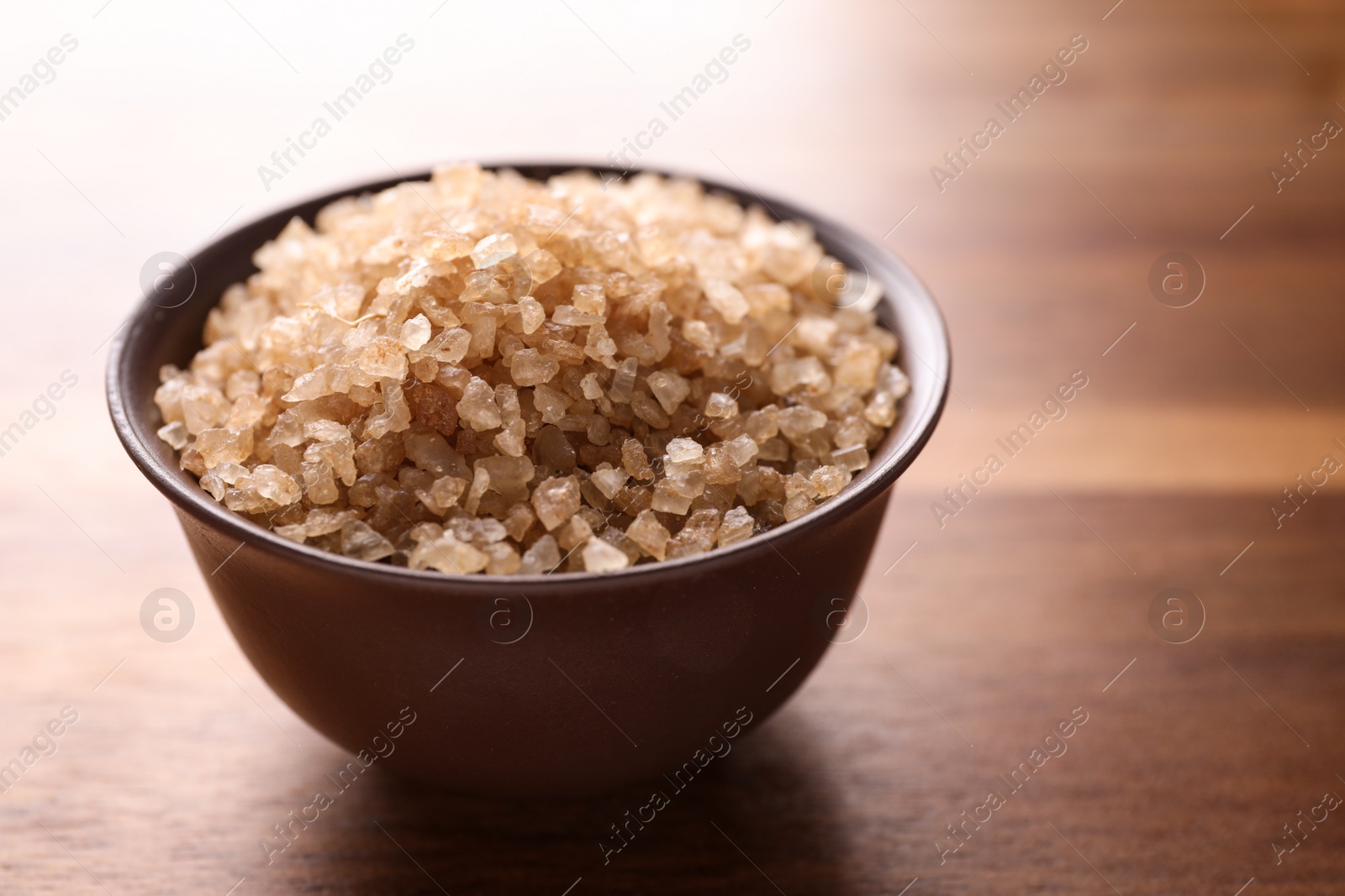 Photo of Bowl with brown sea salt on wooden table, closeup. Spa treatment