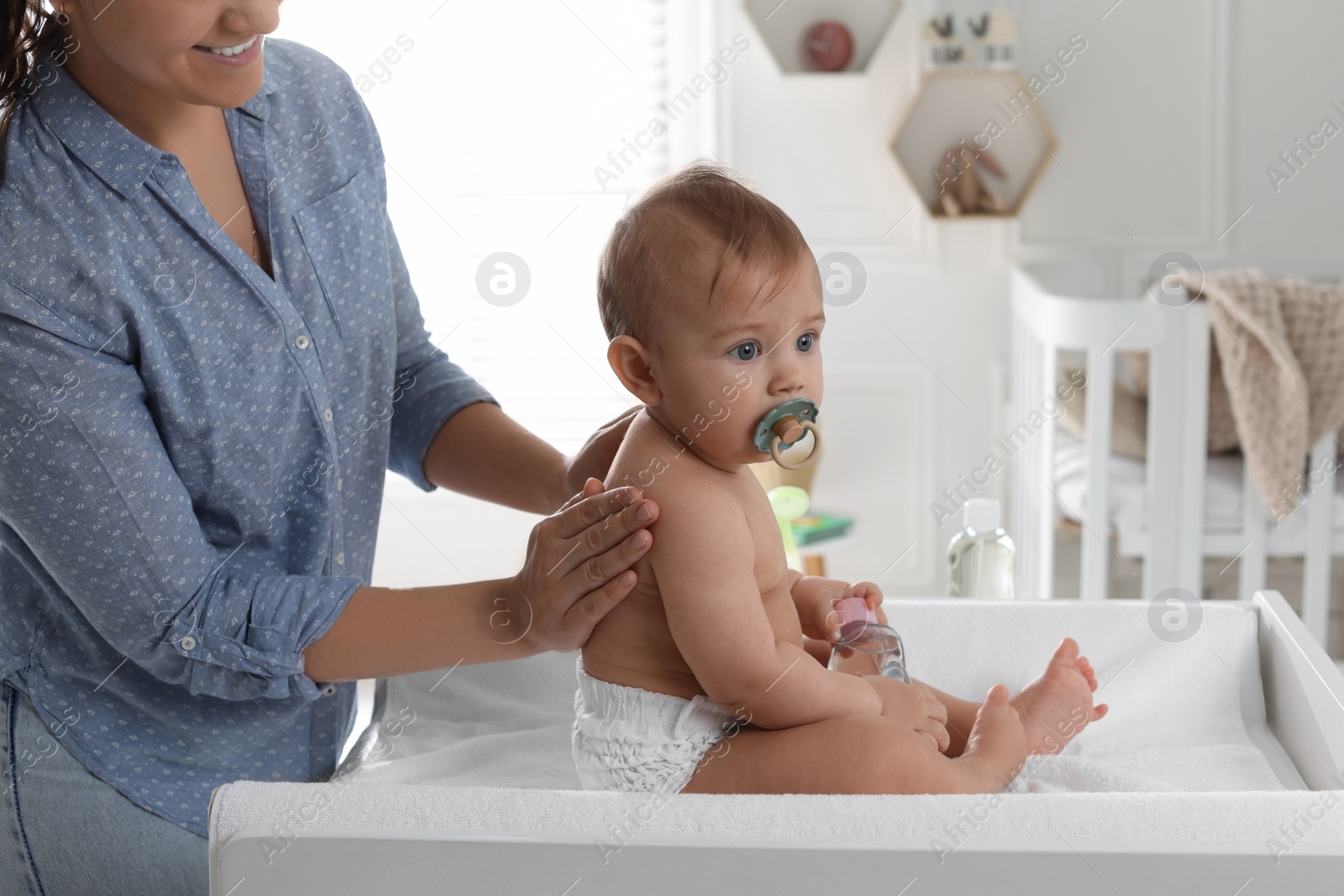 Photo of Mother massaging her cute baby with oil on changing table at home, closeup