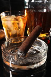 Photo of Smoldering cigar, ashtray and whiskey on black mirror surface, closeup