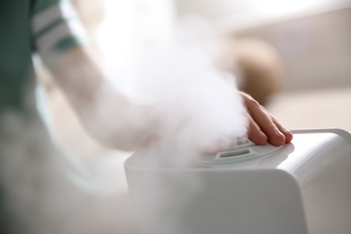 Woman using modern air humidifier at home, closeup