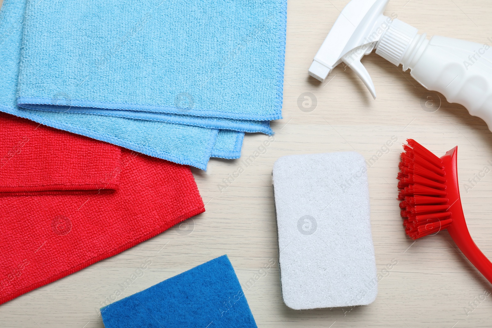 Photo of Microfiber cloths and cleaning supplies on light wooden background, flat lay