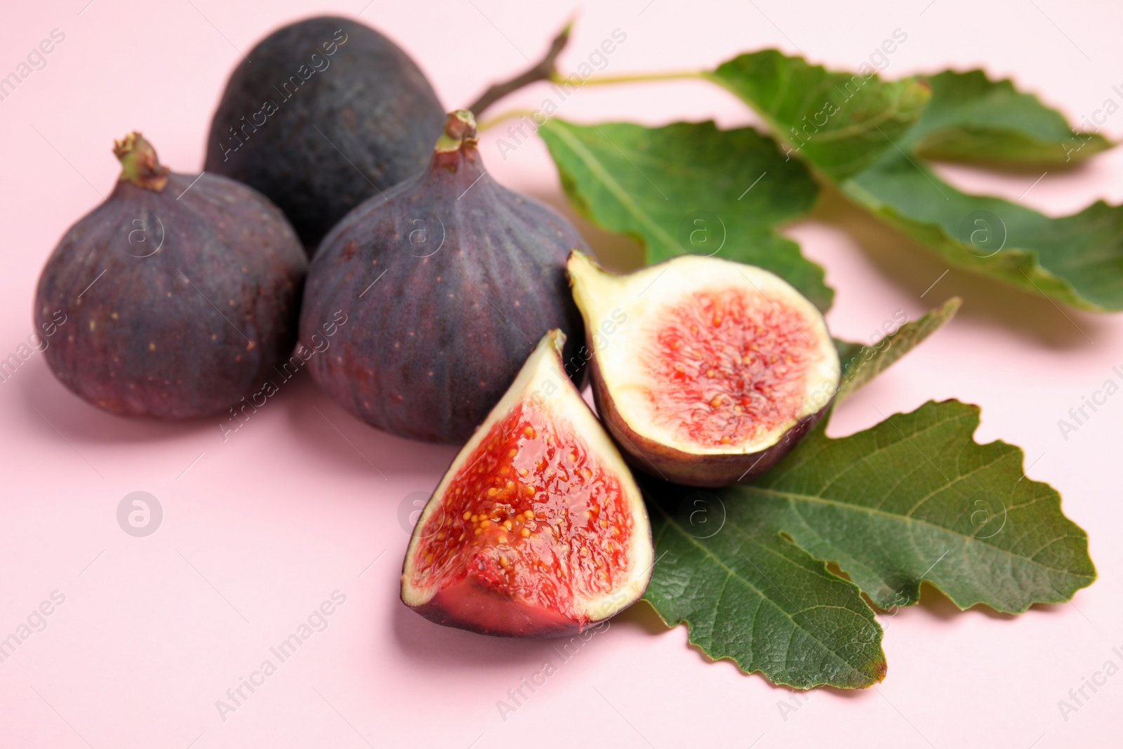 Photo of Delicious ripe figs and green leaves on pink background, closeup