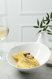 Photo of Tasty capellini with mussels and lemon served on light grey table. Exquisite presentation of pasta dish