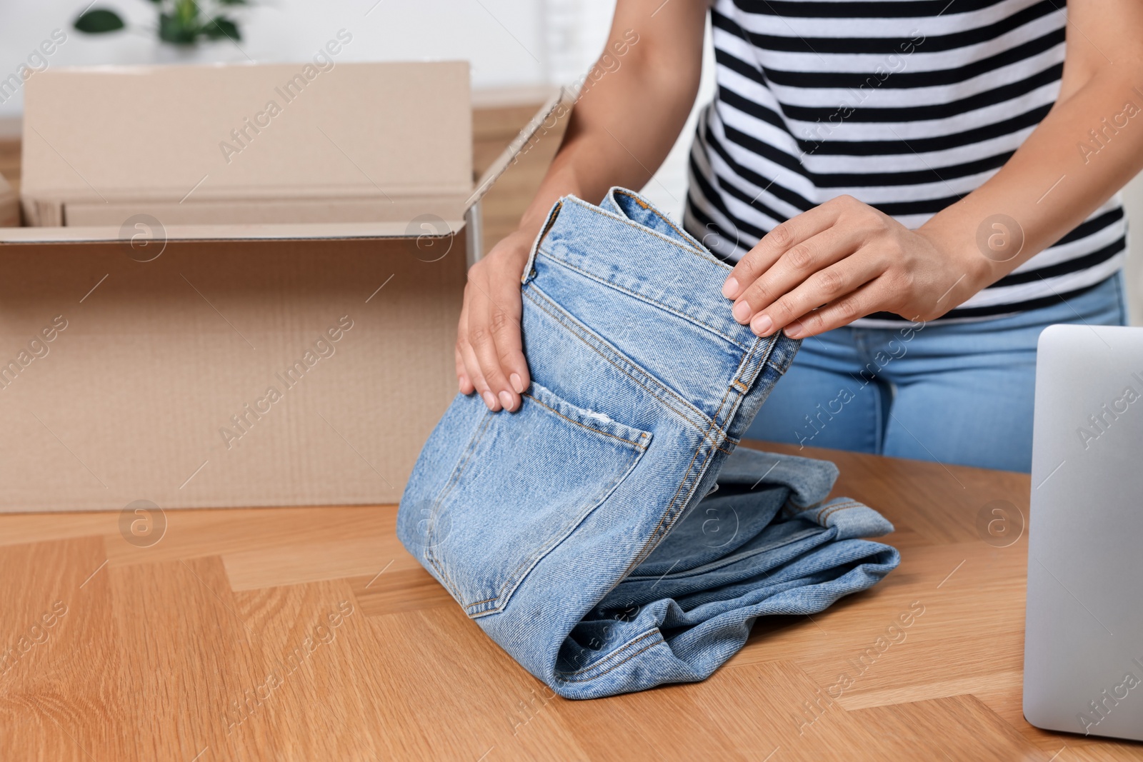 Photo of Young woman with just unpacked new jeans at wooden table indoors, closeup and space for text. Online shopping