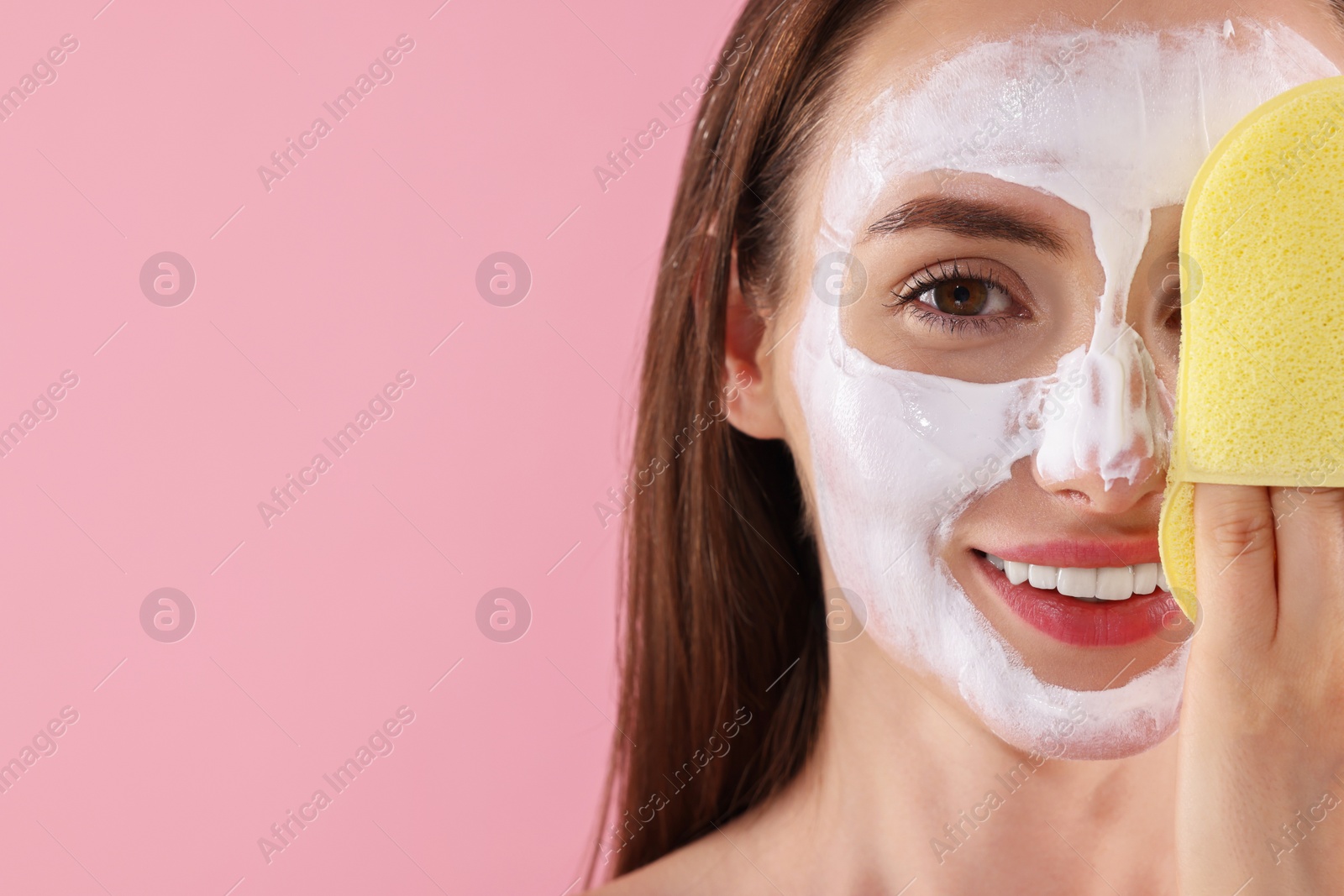 Photo of Happy young woman with face mask and sponge on pink background, closeup Space for text