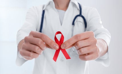 Cancer awareness. Doctor holding red ribbon on blurred background, closeup. Banner design