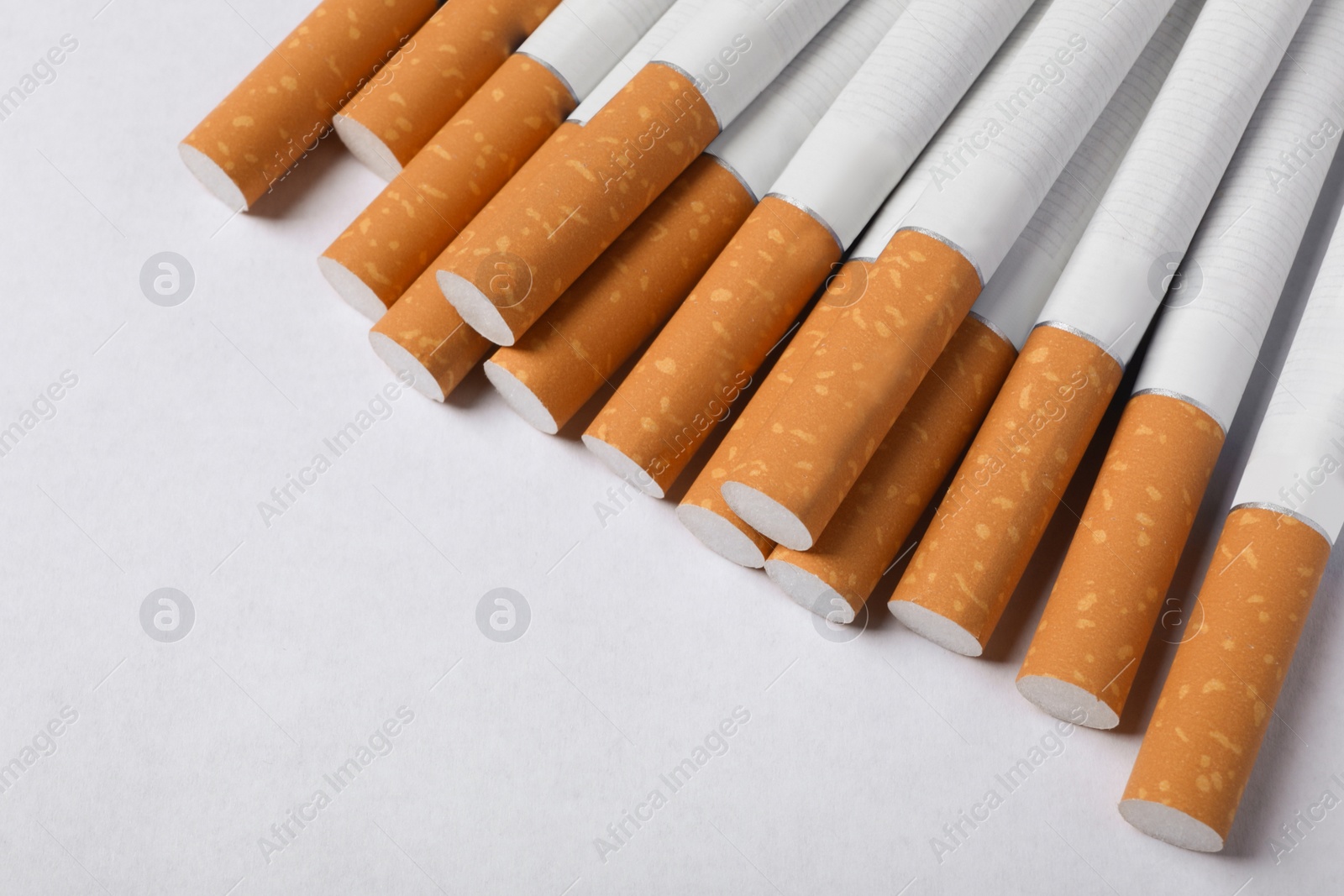 Photo of Pile of cigarettes with orange filters on white background, above view. Space for text