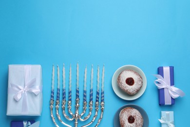 Flat lay composition with Hanukkah menorah and donuts on light blue background, space for text