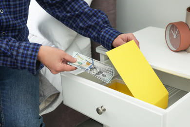 Photo of Man hiding dollar banknotes in cabinet indoors, closeup. Money savings