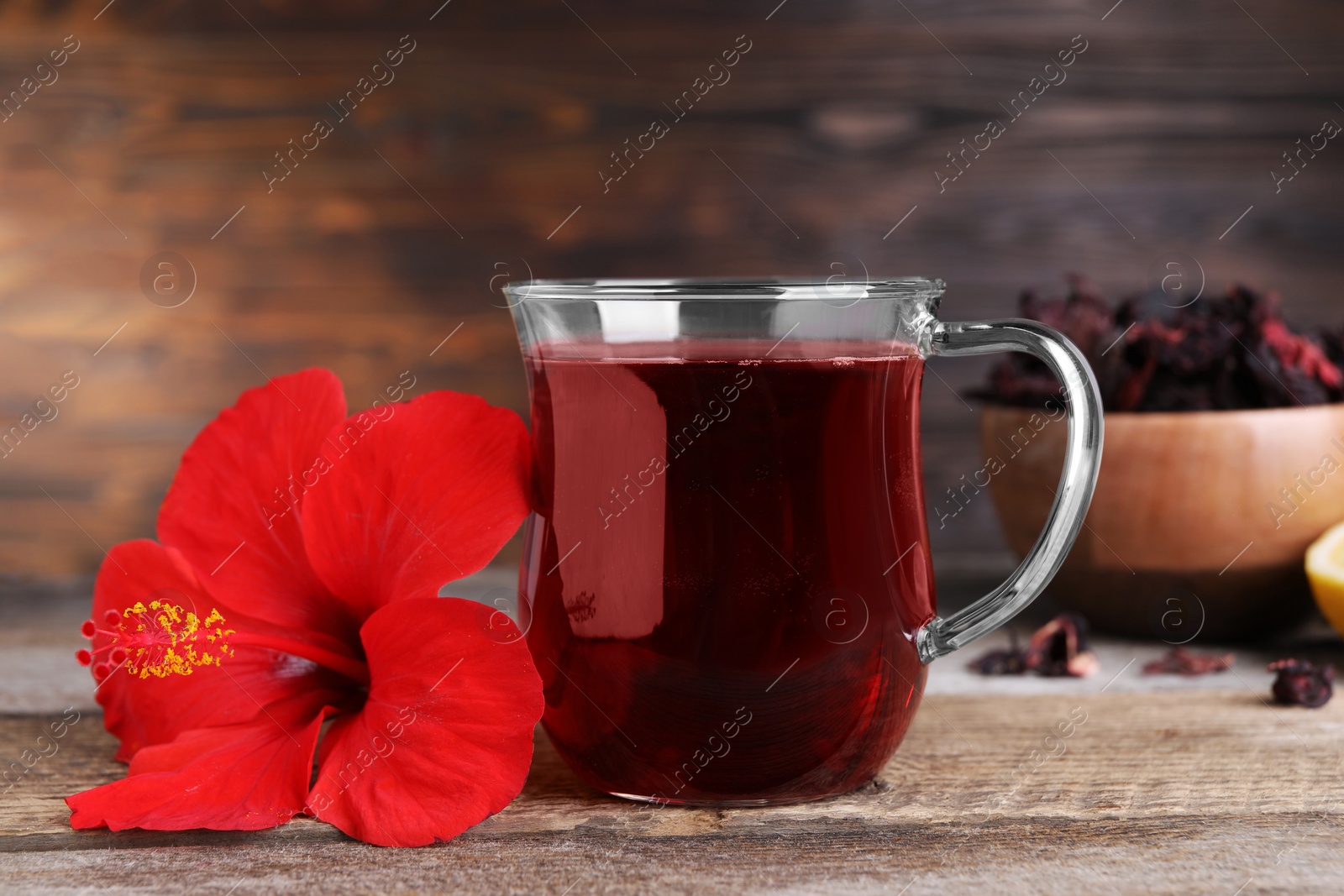 Photo of Delicious hibiscus tea and beautiful flower on wooden table, closeup