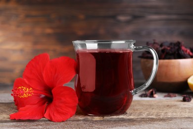 Delicious hibiscus tea and beautiful flower on wooden table, closeup