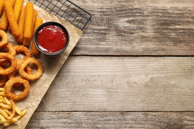 Tasty ketchup and different snacks on wooden table, top view. Space for text