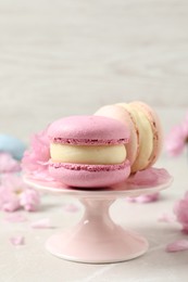 Photo of Delicious colorful macarons and pink flowers on light grey table