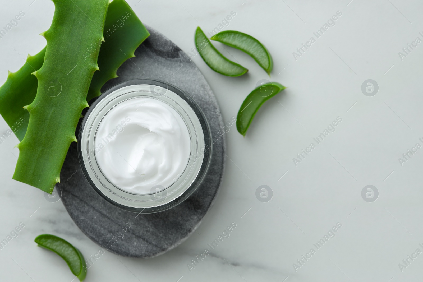 Photo of Jar with cream and cut aloe leaves on white marble table, flat lay. Space for text