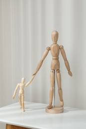 Photo of Wooden mannequins of parent with child on white table against light background. Family Day