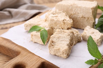 Photo of Pieces of tasty halva and mint leaves on wooden table, closeup