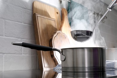 Adding water with ladle into steaming saucepan on stove in kitchen