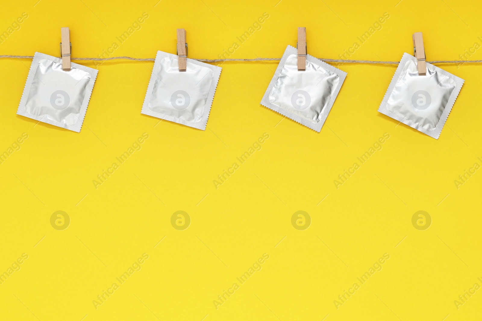 Photo of Clothesline with packaged condoms on yellow background, space for text. Safe sex