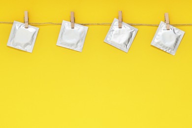 Photo of Clothesline with packaged condoms on yellow background, space for text. Safe sex