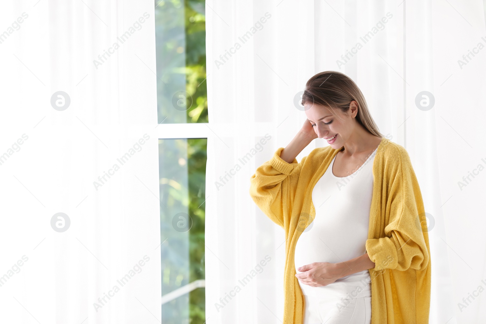 Photo of Happy pregnant woman standing near window at home