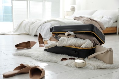 Photo of Open suitcase full of clothes, shoes and fashionable accessories on floor in bedroom