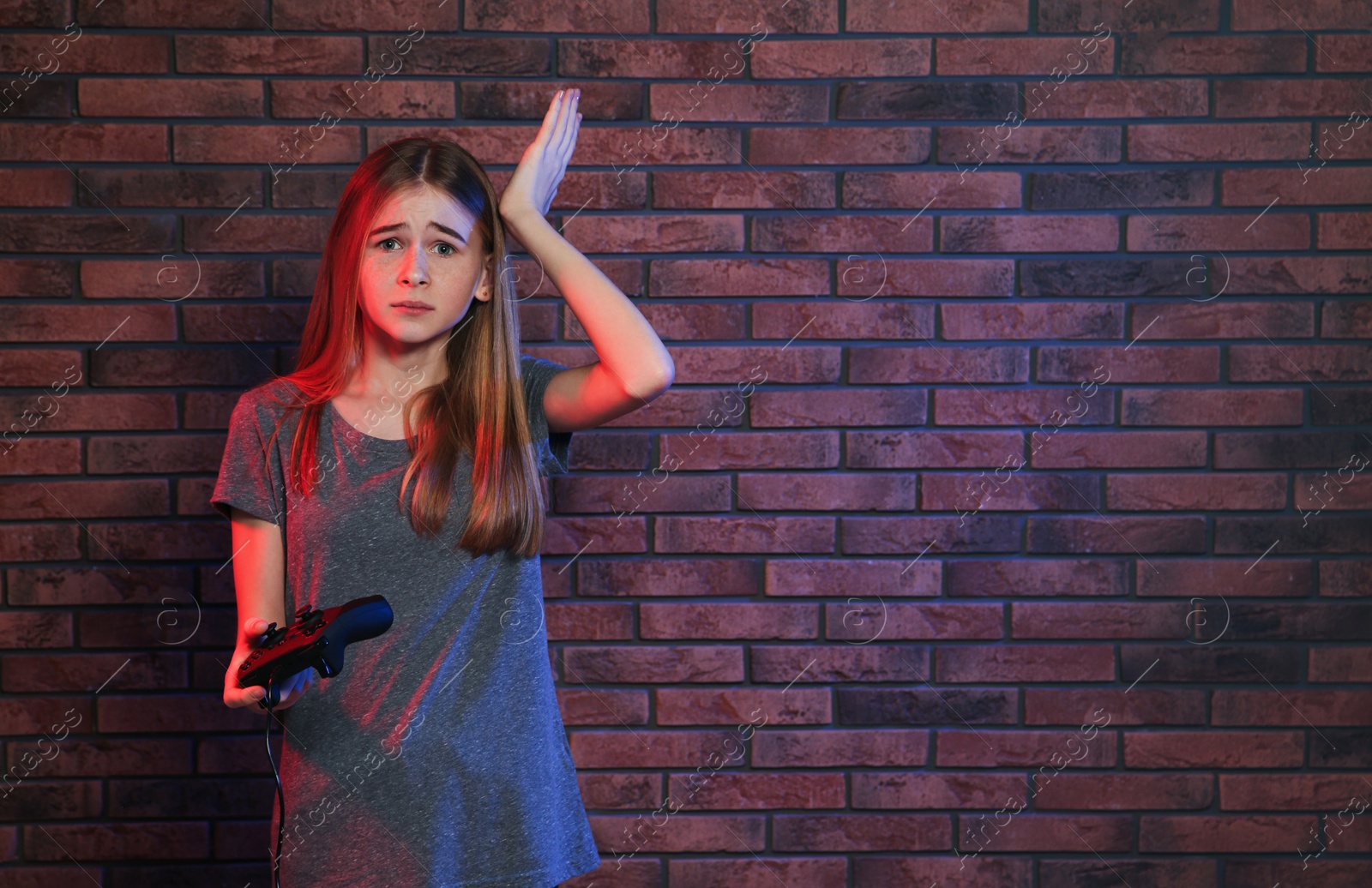 Photo of Teenage girl playing video games with controller near brick wall. Space for text