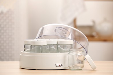 Photo of Modern yogurt maker with empty jars on table indoors