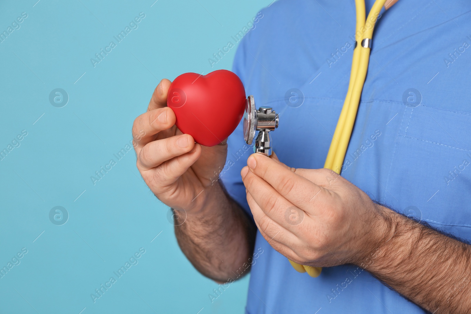 Photo of Doctor with stethoscope and red heart on light blue background, closeup. Cardiology concept