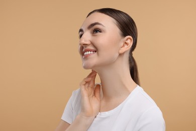 Smiling woman touching her neck on beige background