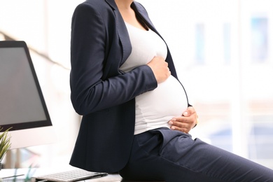 Photo of Young pregnant woman in suit at workplace, closeup