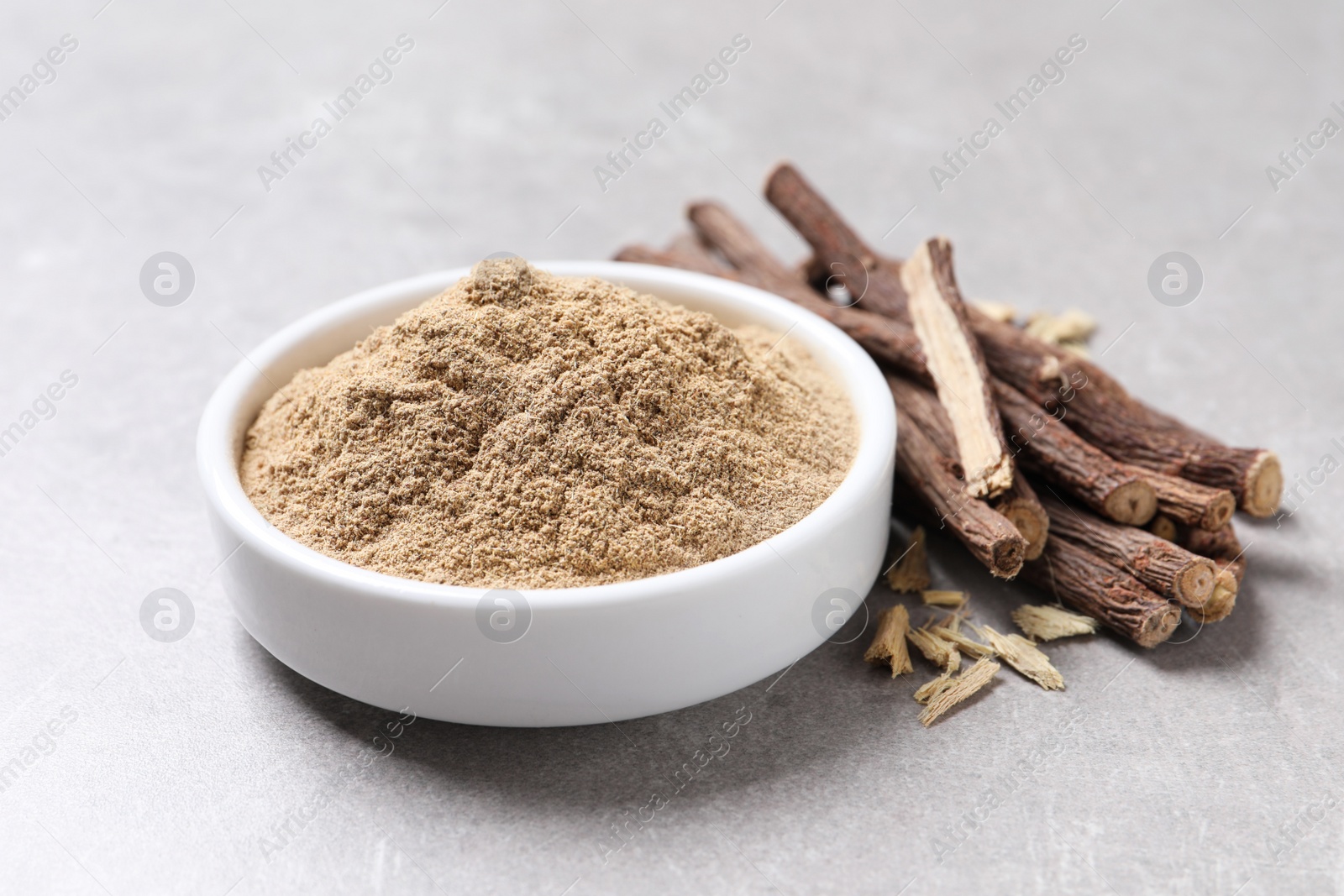 Photo of Dried sticks of liquorice root and powder on grey table, closeup