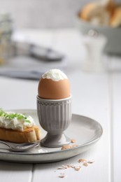 Photo of Fresh soft boiled egg in cup and sandwich on white wooden table