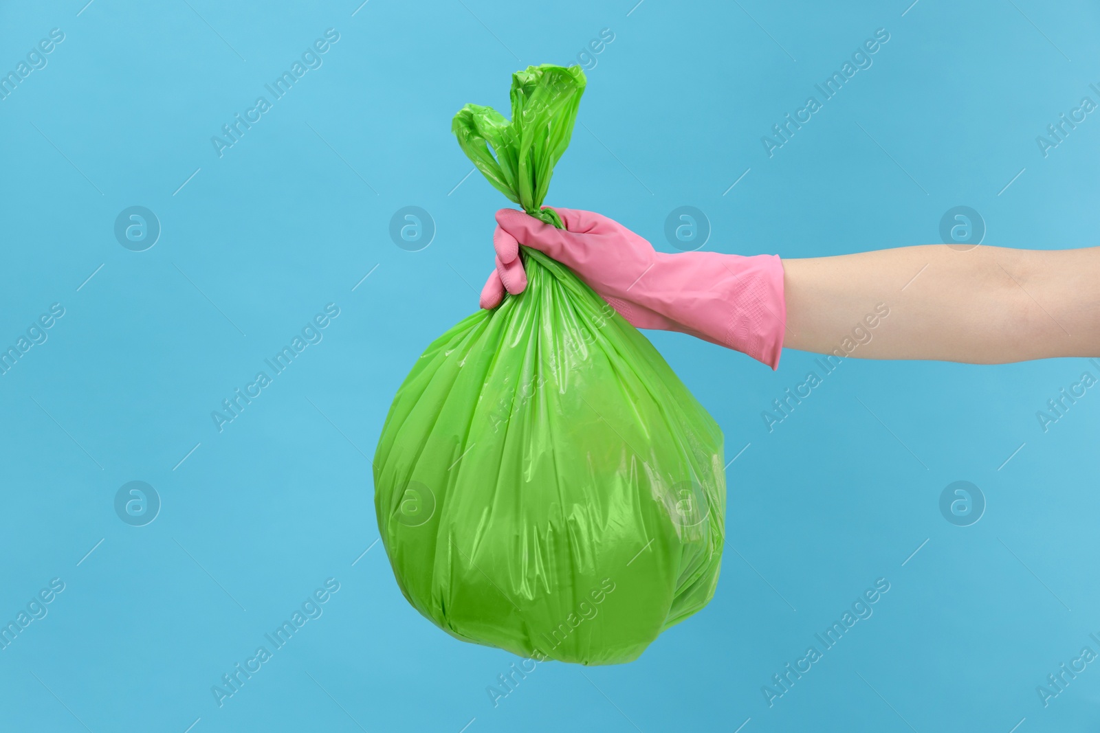 Photo of Woman holding plastic bag full of garbage on light blue background, closeup