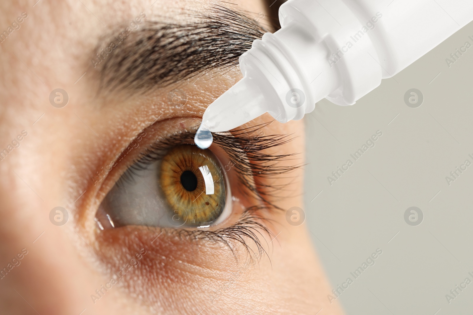 Image of Woman applying eye drops on light background, closeup