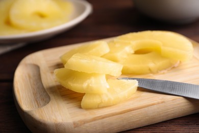 Photo of Canned pineapple pieces and knife on wooden board, closeup