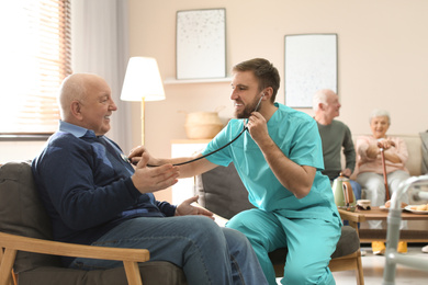 Photo of Care worker examining elderly patient with stethoscope in geriatric hospice