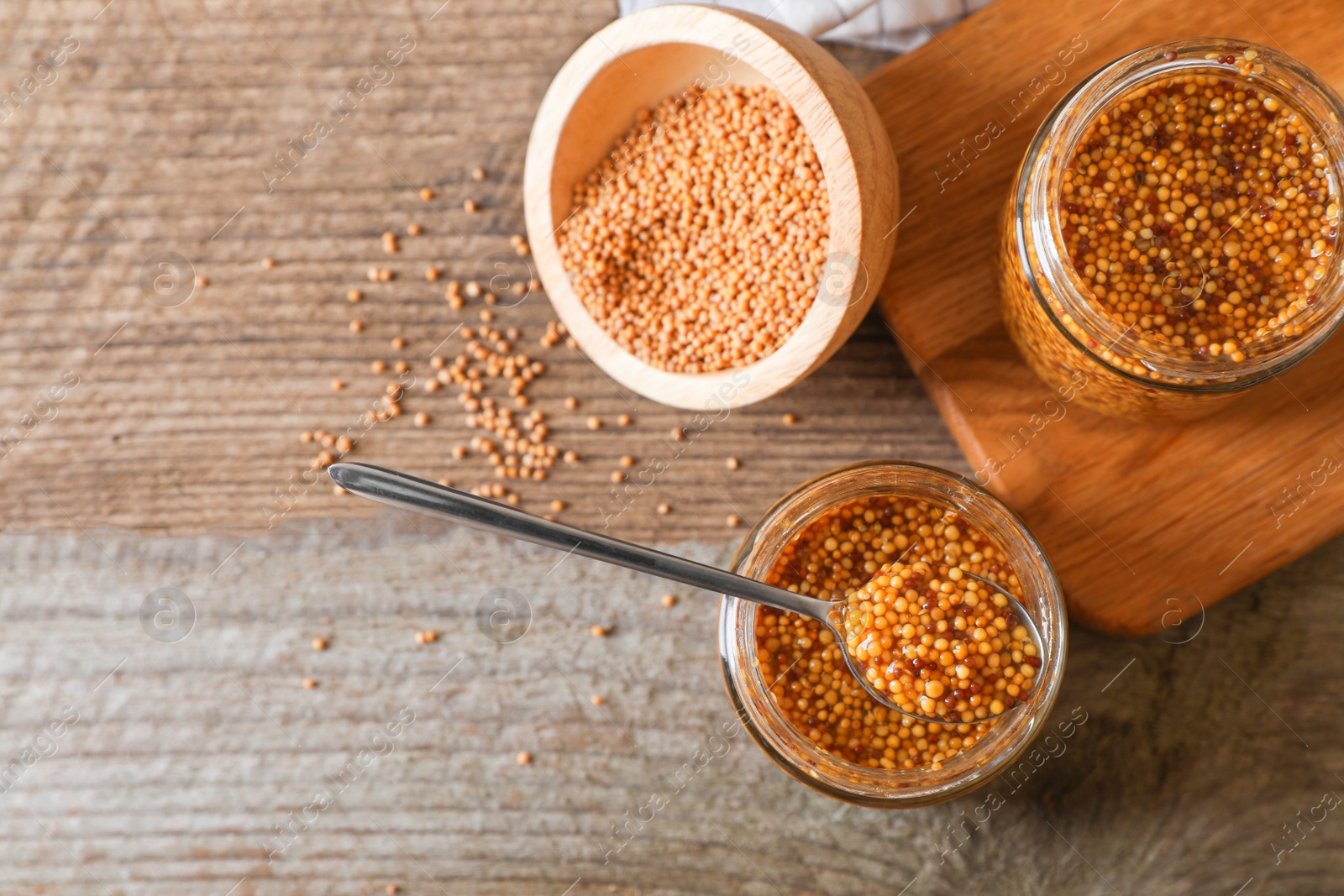 Photo of Bowl and jars of whole grain mustard on wooden table, flat lay. Space for text