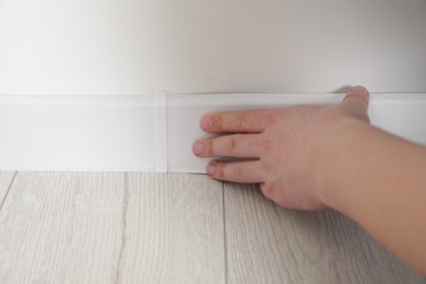 Photo of Man installing plinth on laminated floor in room, closeup