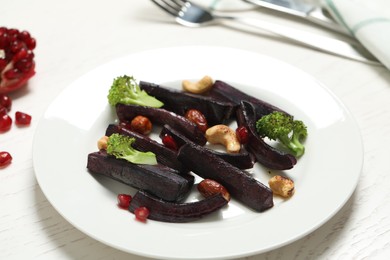 Photo of Tasty raw black carrot with broccoli and nuts on white table, closeup