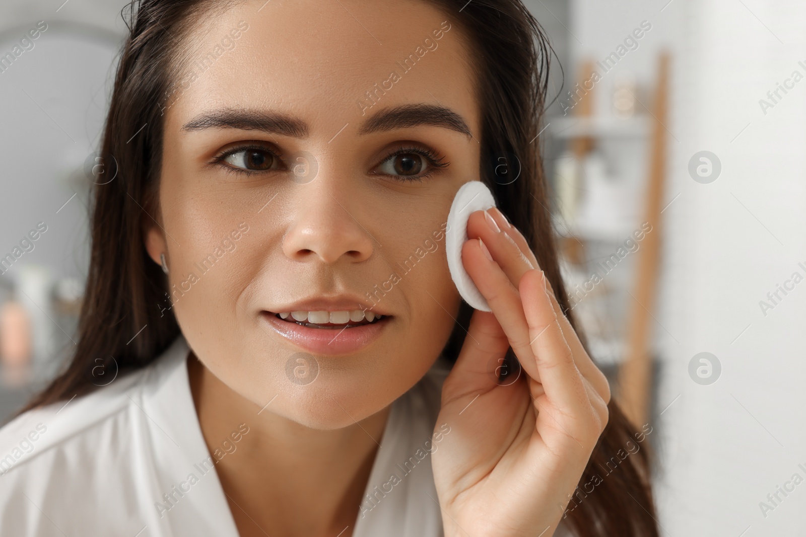 Photo of Young woman cleaning her face with cotton pad in bathroom, closeup