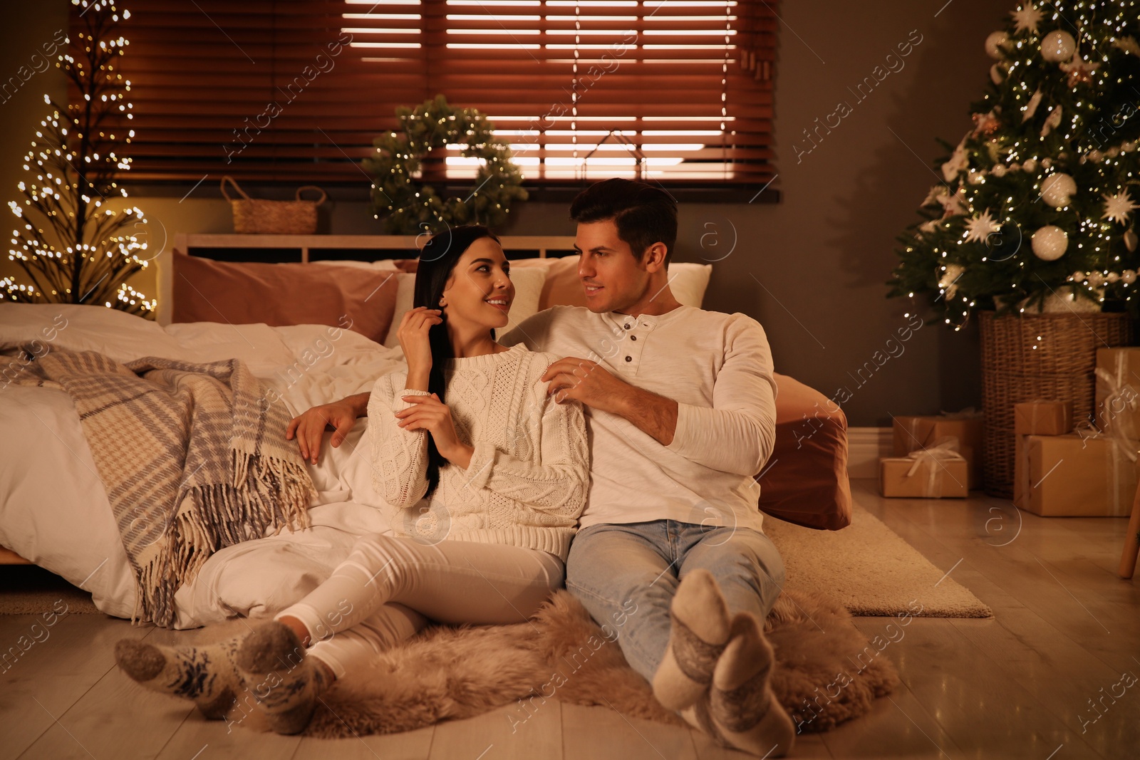 Photo of Happy couple sitting in festively decorated bedroom. Christmas celebration