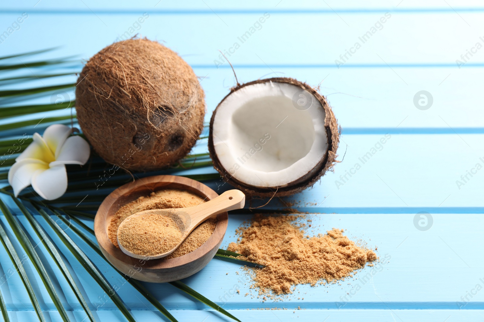 Photo of Coconut sugar, palm leaves, fruits and flower on light blue wooden table, closeup