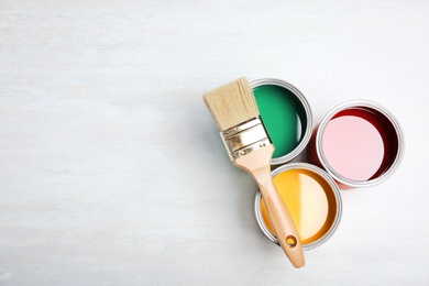 Photo of Cans with paint and brush on light background, top view. Space for text