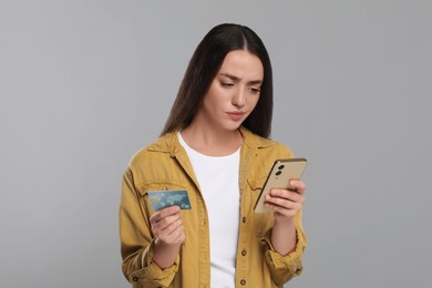 Photo of Confused woman with credit card and smartphone on light gray background. Debt problem