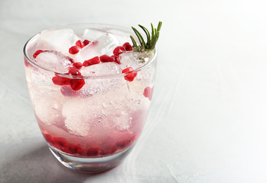 Photo of Tasty cocktail with ice cubes and pomegranate on light grey table, closeup. Space for text